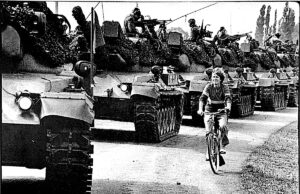 Io li sorpasso Carovane di carri armati durante un corteo storico, donna in bicicletta in primo piano, scena di protest and memoria storica.